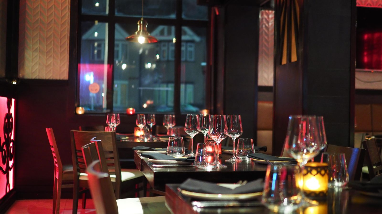 The dim candlelit dining room of NOIR, wine glasses catching low golden light on dark oak tables